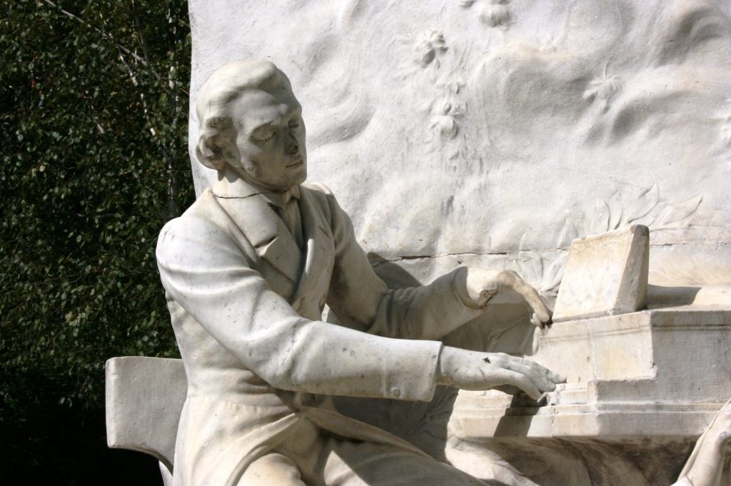 Marble statue of Frederic Chopin seated at a piano, close-up on hands and keys, outdoor monument.