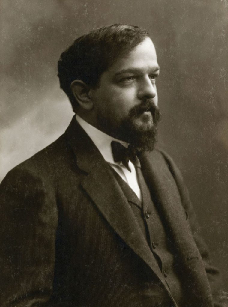 A rare historical black and white portrait of Claude Debussy, French Impressionist composer, seated in a formal suit, circa 1908. High-resolution public domain image.